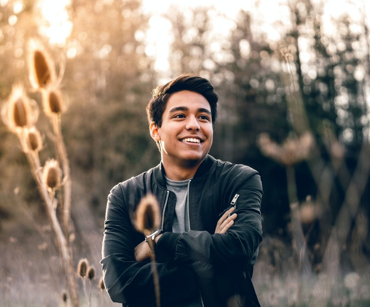 Hispanic man standing in a field with his arms crossed, smiling.